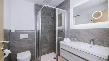 Modern bathroom with shower, sink, mirror, towels, and toilet in neutral tones.