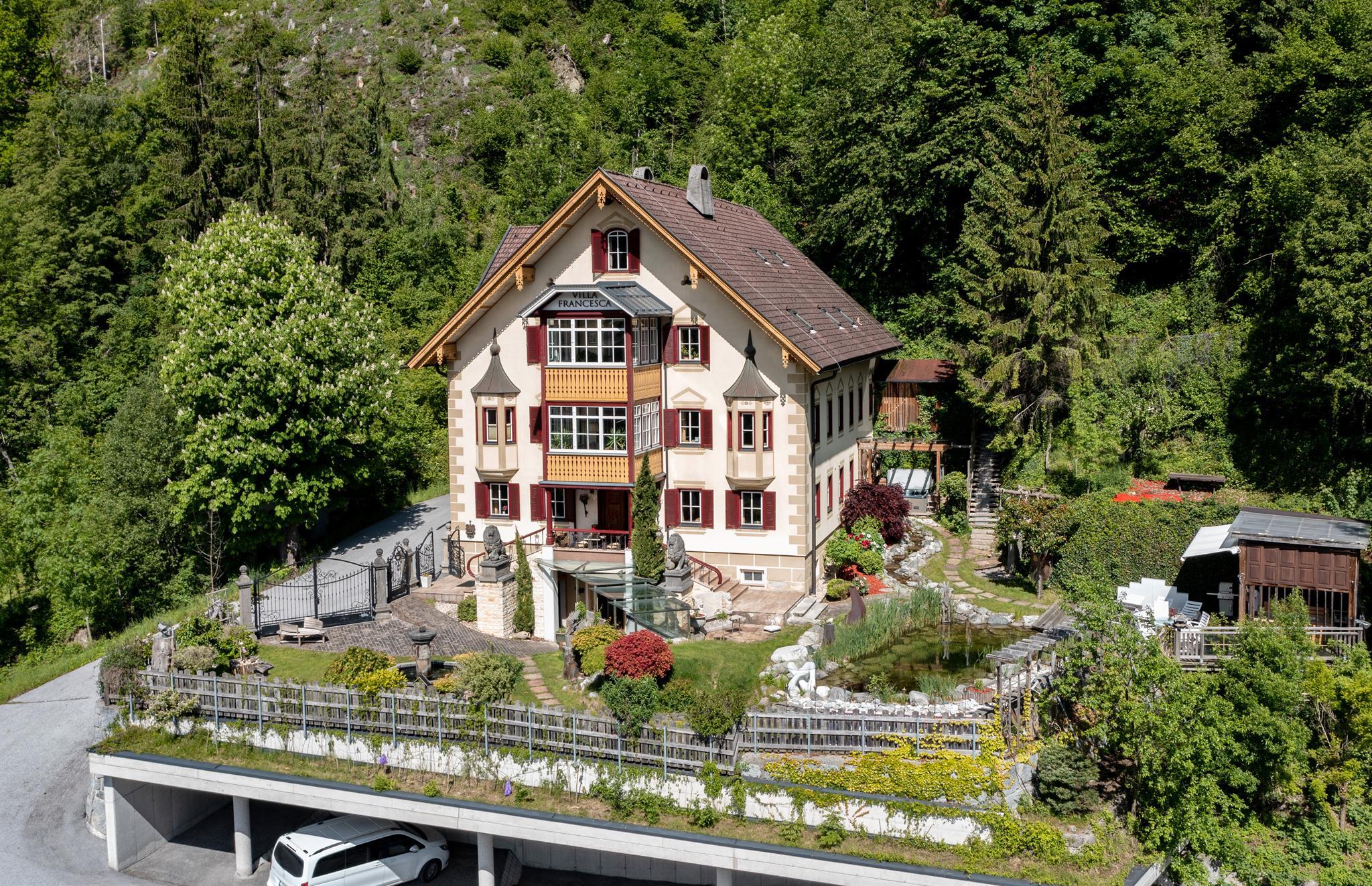 House surrounded by trees and garden, with a car underpass at the bottom.