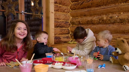 Four children are sitting at a table decorating gingerbread cookies.