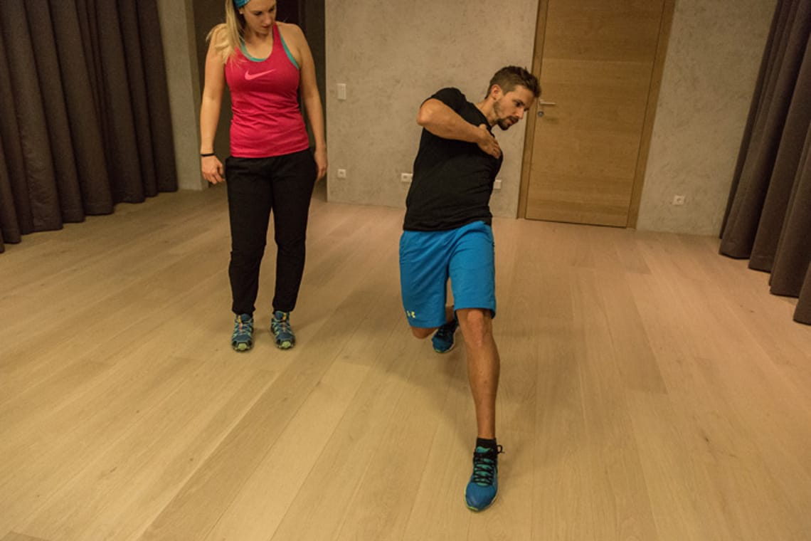 Diagonal Stretch - Chris Ebenbichler Man performing diagonal stretch exercise in training room in Mayrhofen, observed by training partner. Christoph Ebenbichler demonstrates movement to improve balance, mobility and coordination for ski fitness.
