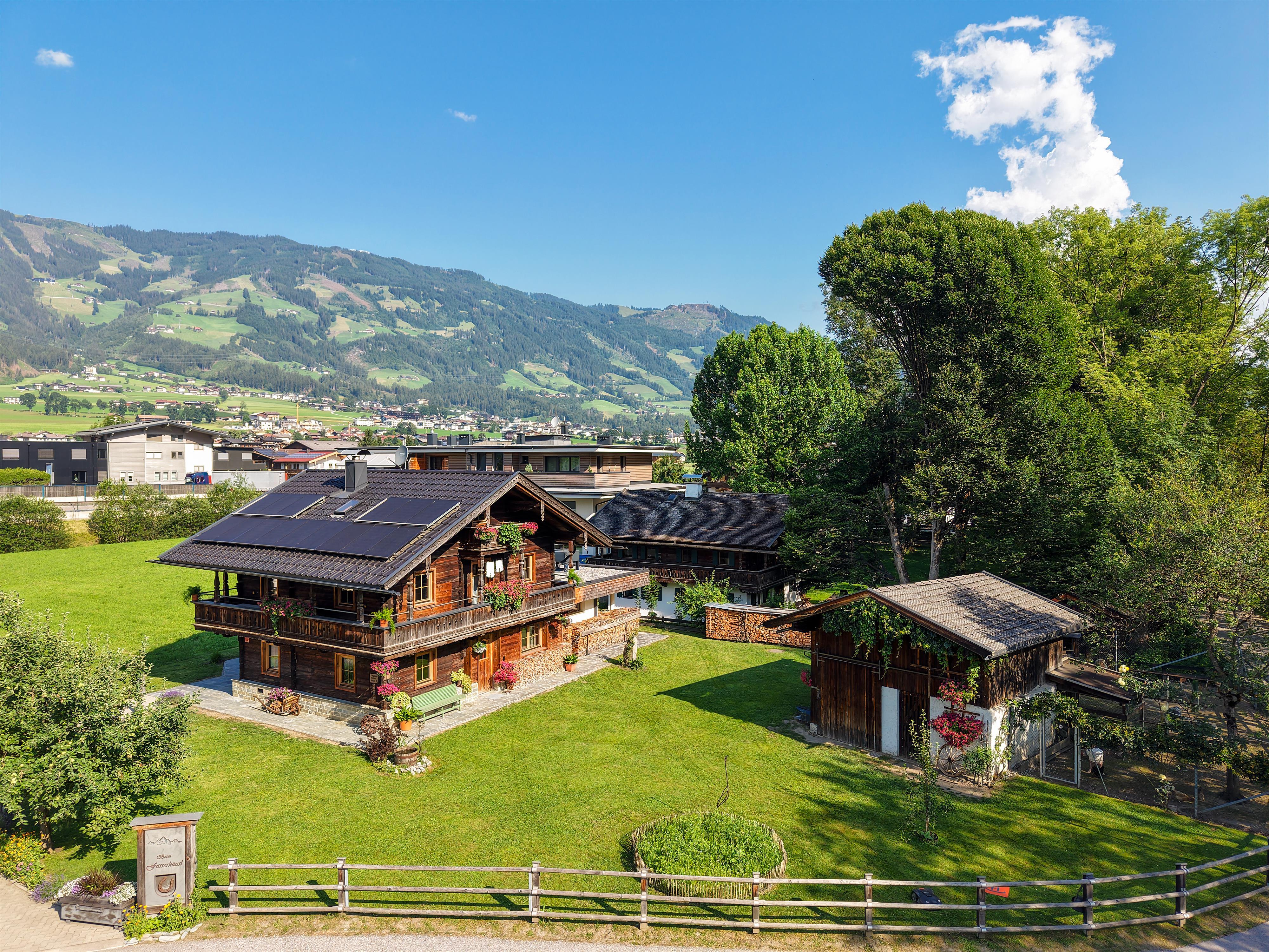 Traditionelles Chalet mit Blumen am Balkon, umgeben von grünen Wiesen und Bäumen in einer Bergregion.