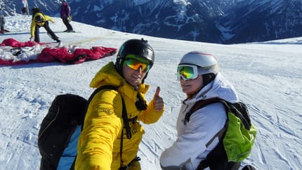 Zwei Skifahrer in Winterkleidung auf verschneitem Berg mit Bergen im Hintergrund, einer gibt Daumen hoch.