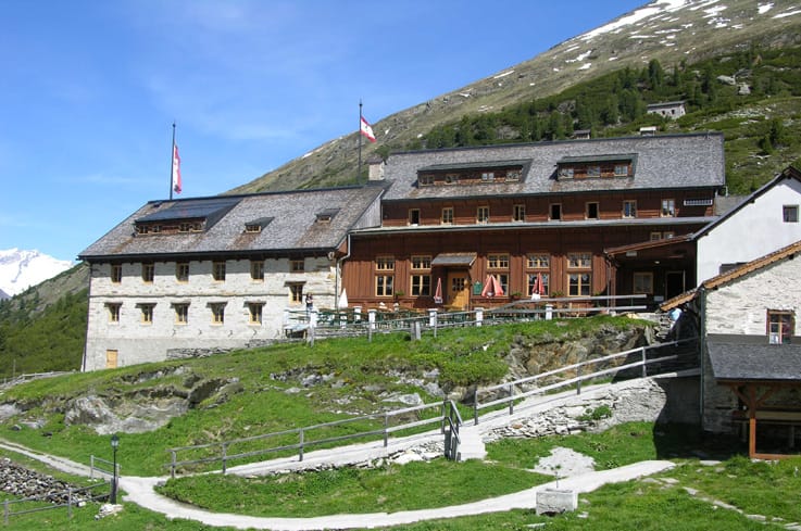 Berliner Hütte in Zillertal Valley The Berliner Hütte in the Zillertal Alps Nature Park, a historic mountain hut in the Mayrhofen-Hippach holiday region. The impressive stone and wood refuge is set in an alpine landscape with green meadows and snow-covered peaks.