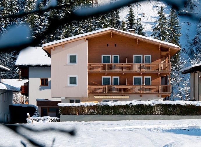 Mehrstöckiges Haus in verschneiter Berglandschaft mit Holz- und Putzfassade, umgeben von Tannenbäumen.