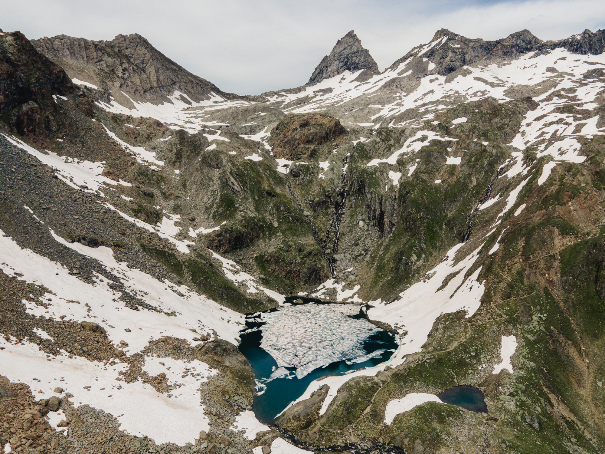 Mountain landscape with snow-covered peaks, valleys, and a glacier lake in the foreground.