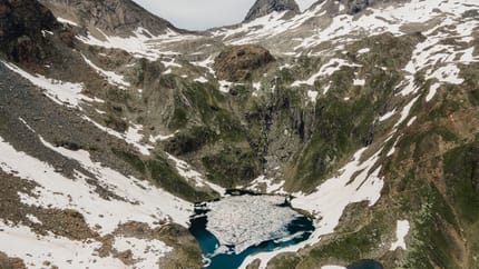 Mountain landscape with snow-covered peaks, valleys, and a glacier lake in the foreground.