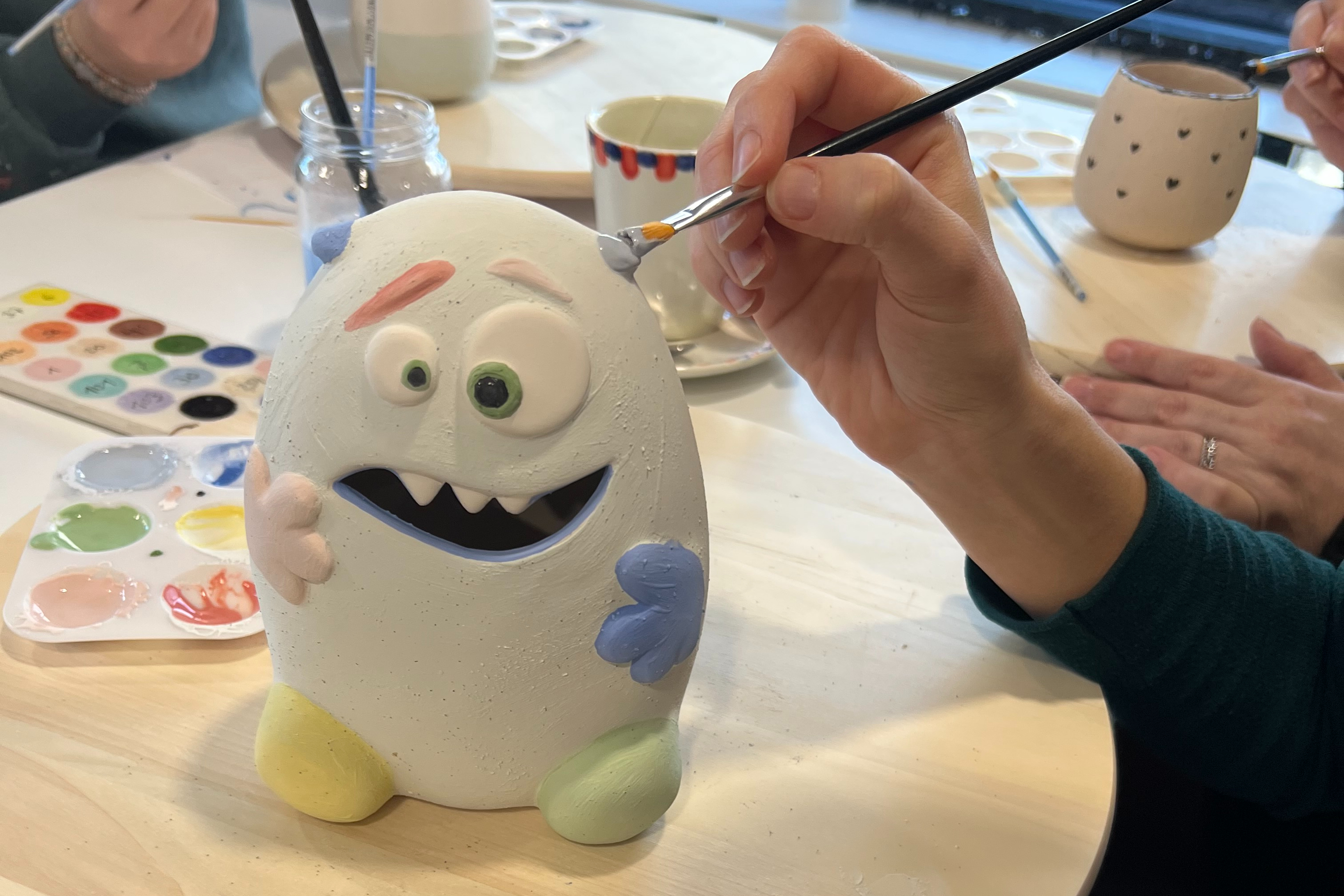 A ceramic piece that looks like a monster is being painted by a person holding a brush.