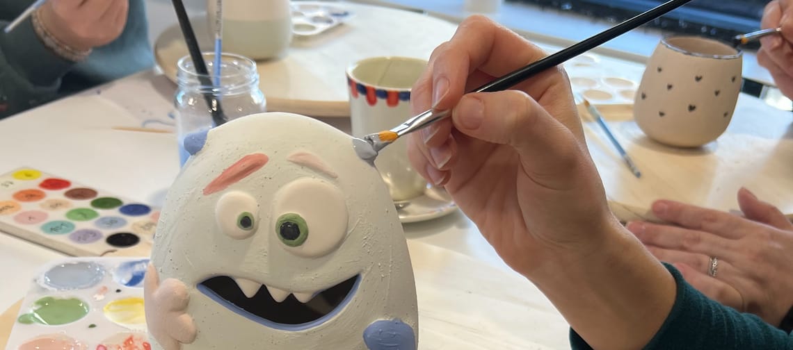A ceramic piece that looks like a monster is being painted by a person holding a brush.