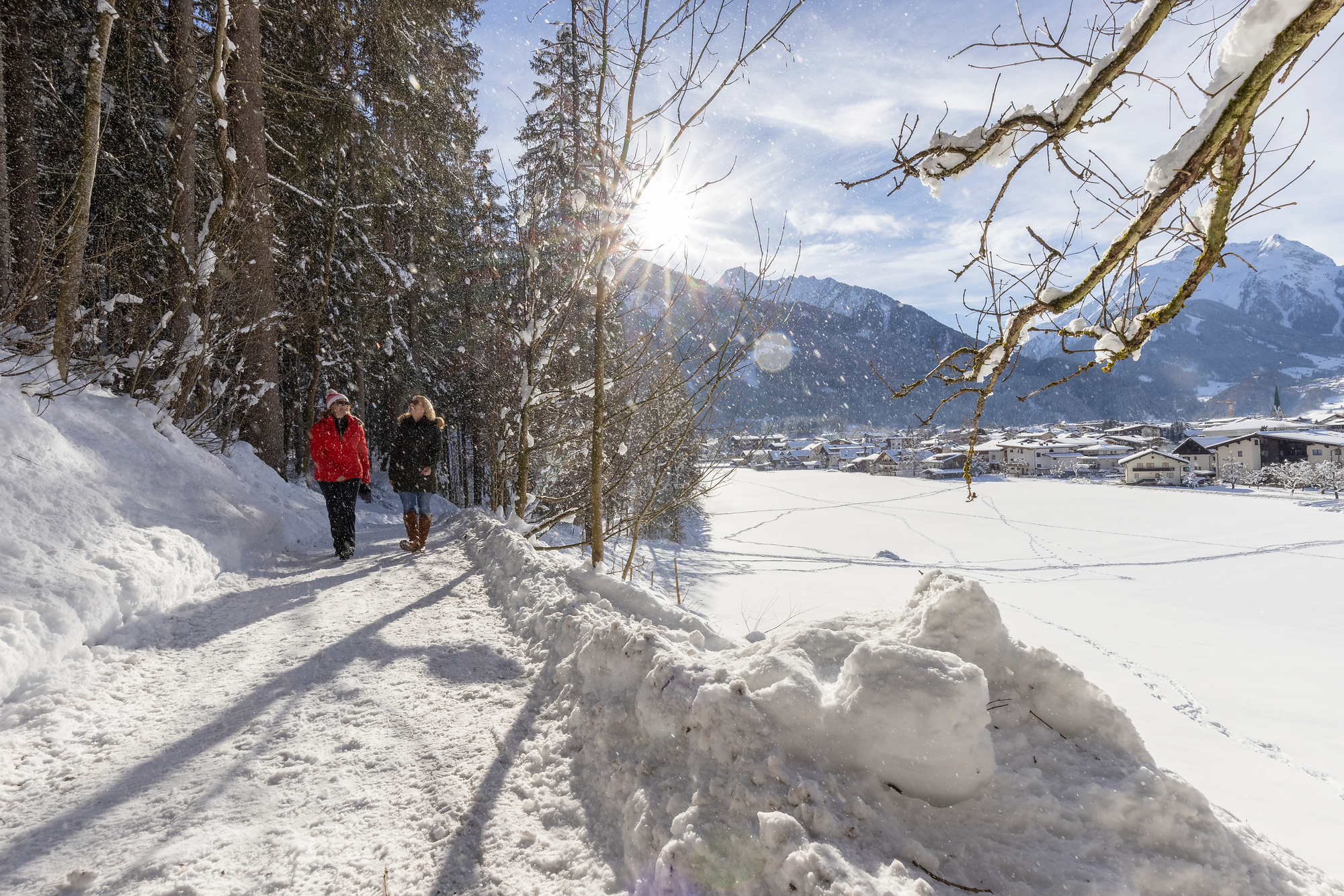 Zwei Personen beim Winterwandern am verschneiten Easy Trail bei Mayrhofen-Hippach, mit Blick auf die Zillertaler Alpen und Blick auf den Ort Mayrhofen..