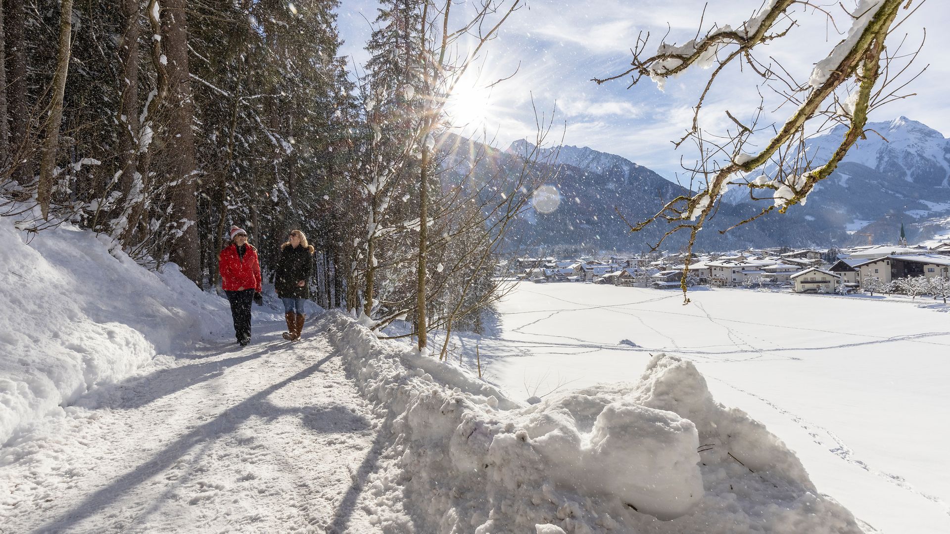 Two people winter hiking on the snow-covered Easy Trail near Mayrhofen-Hippach, Zillertal Alps in the background, sunshine and scenic winter landscape.