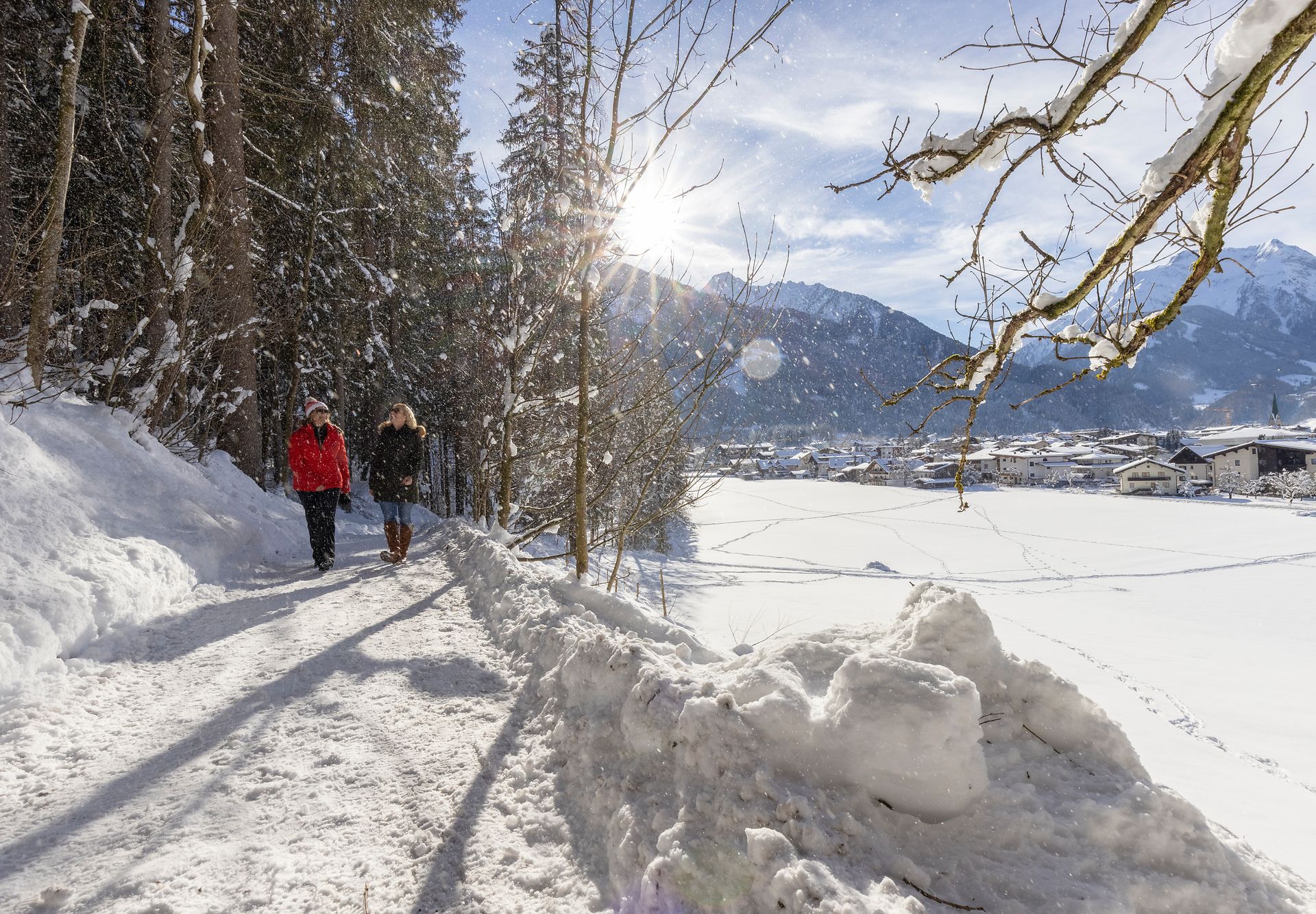 Two people winter hiking on the snow-covered Easy Trail near Mayrhofen-Hippach, Zillertal Alps in the background, sunshine and scenic winter landscape.