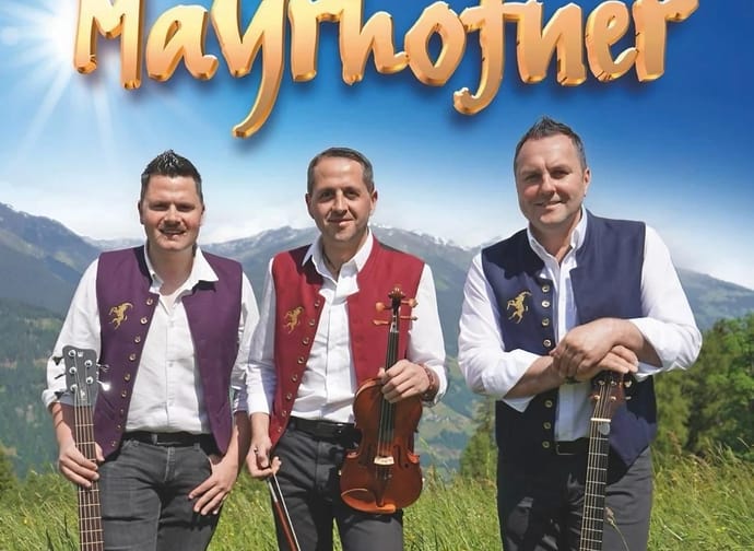 Drei Männer mit Musikinstrumenten vor einer Berglandschaft, tragen traditionelle Trachten, Sonne im Hintergrund.