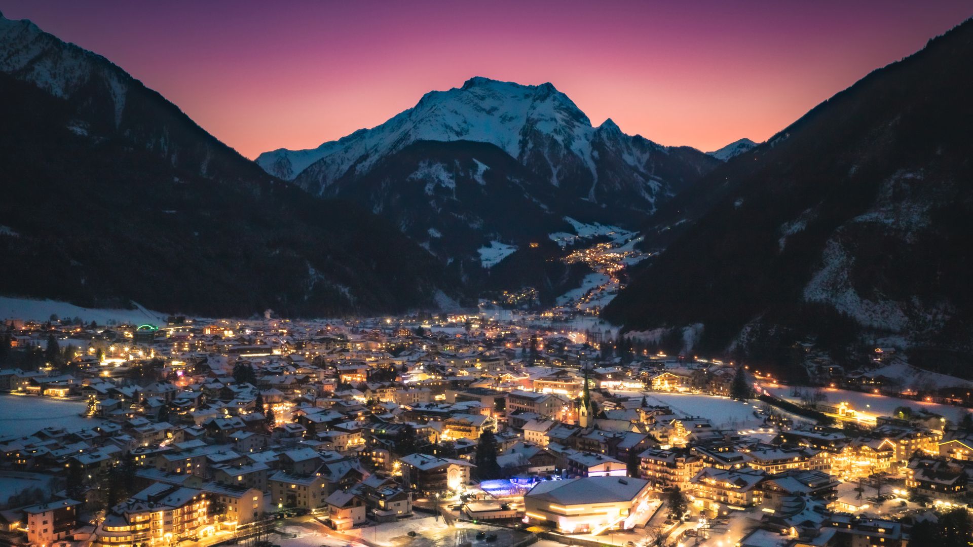 Abendliche Winteraufnahme von Mayrhofen im Zillertal. Das Tal liegt zwischen schneebedeckten Bergen, die Lichter des Ortes leuchten warm in der Dämmerung.