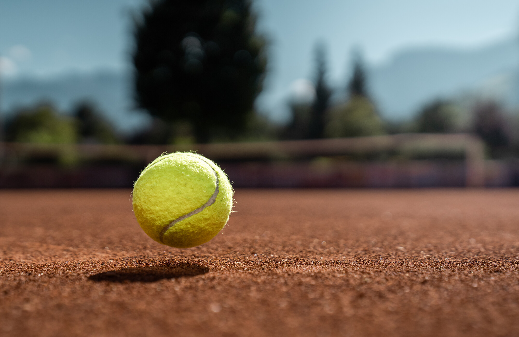 A tennis ball bouncing on a clay court in the Mayrhofen-Hippach holiday region in the Zillertal, Tyrol. Blurred mountains and green nature in the background.