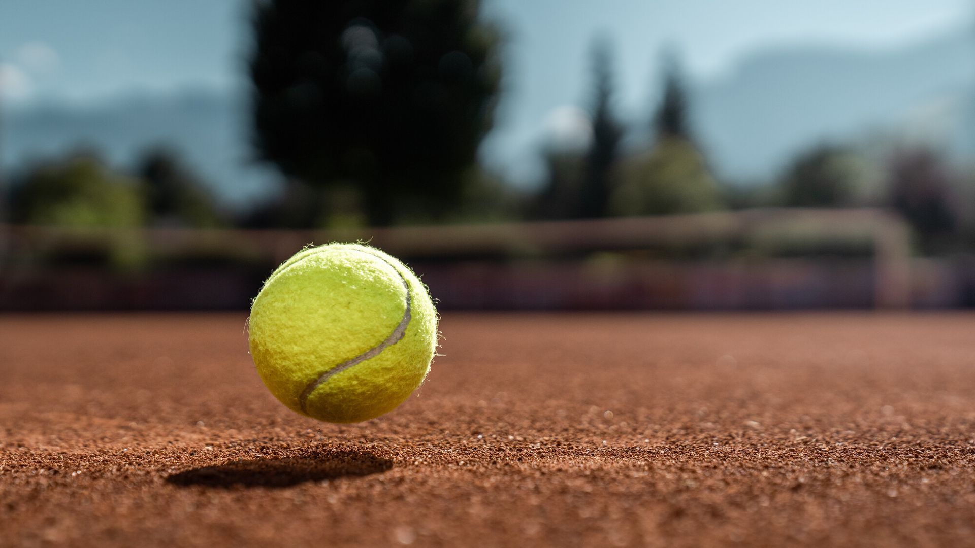 A tennis ball bouncing on a clay court in the Mayrhofen-Hippach holiday region in the Zillertal, Tyrol. Blurred mountains and green nature in the background.