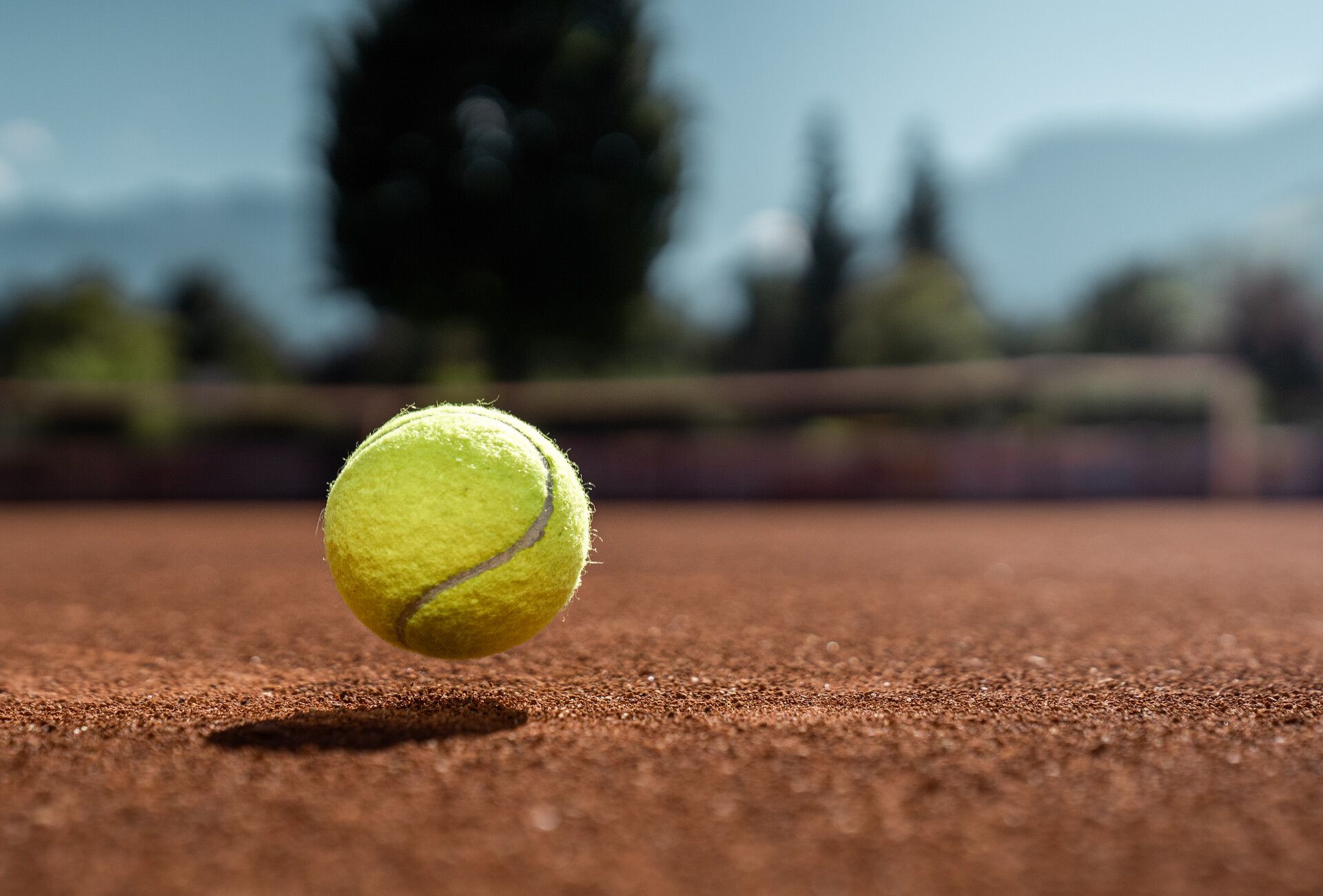 Ein Tennisball springt auf einem Sandplatz in der Ferienregion Mayrhofen-Hippach im Zillertal, Tirol. Im Hintergrund verschwommene Berge und grüne Natur.