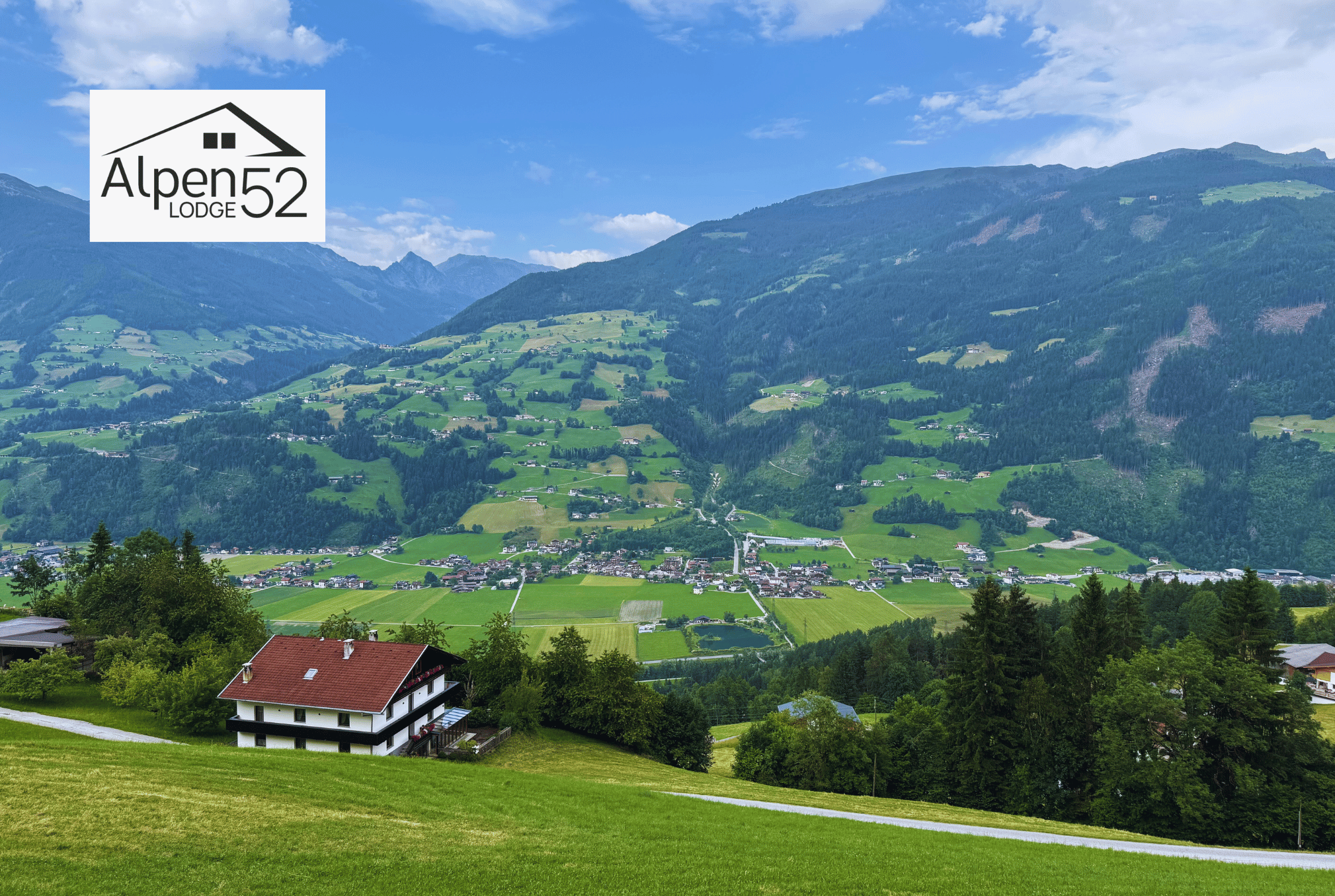 Hütten in einer grünen, bergigen Landschaft unter blauem Himmel mit Wolken.