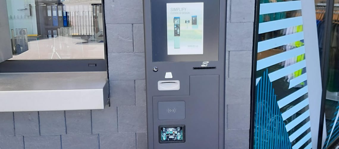 Automatischer Ticket- und Barcode-Scanner vor einer grauen Steinwand, mit digitalem Bildschirm und Kartenleser.