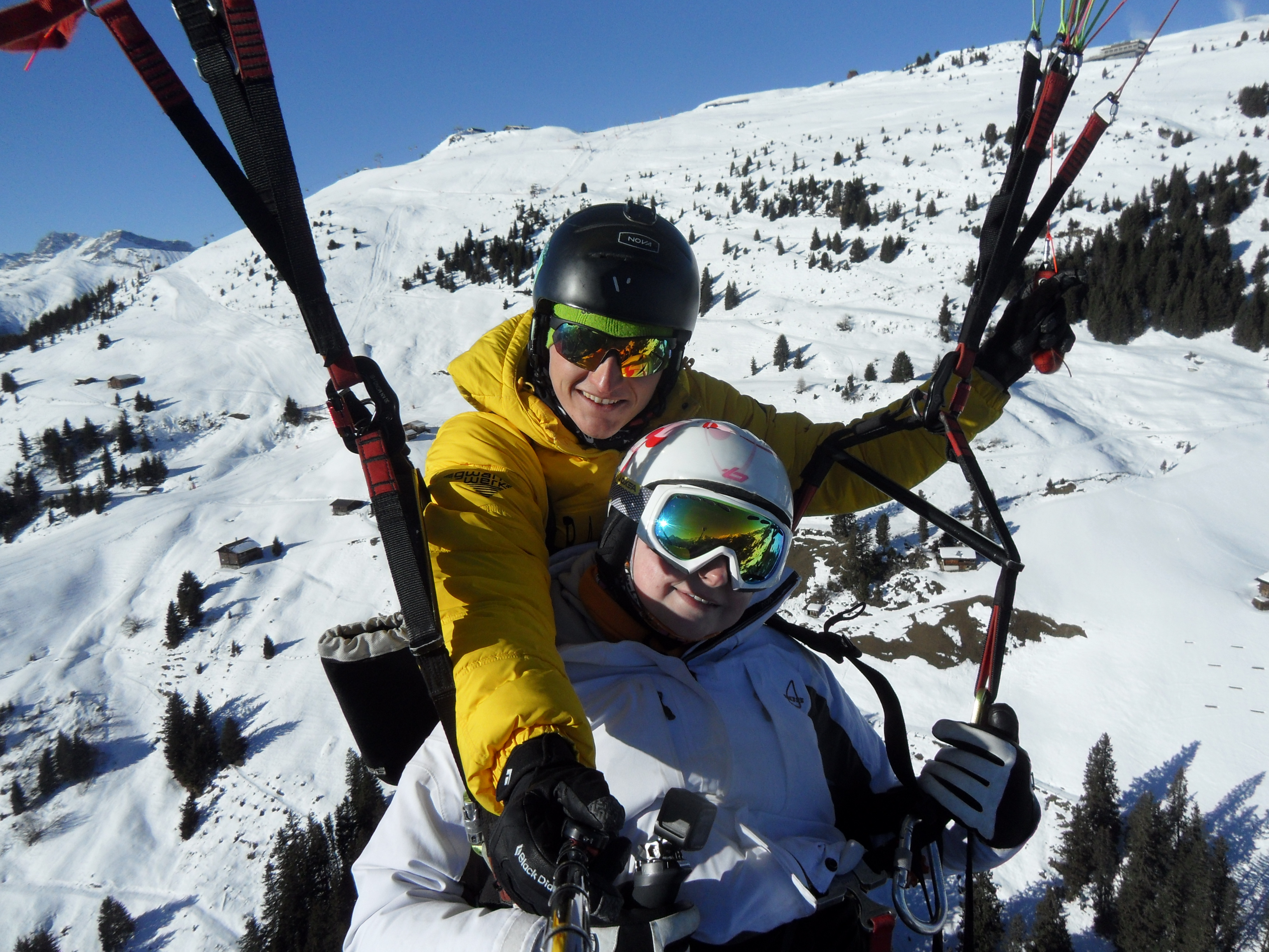 Zwei Skifahrer auf Schneelandschaft, einer trägt einen schwarzen Helm und gelbe Jacke, beide mit Skibrille, im Gebirge.
