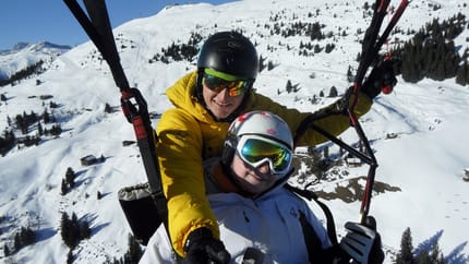Zwei Skifahrer auf Schneelandschaft, einer trägt einen schwarzen Helm und gelbe Jacke, beide mit Skibrille, im Gebirge.