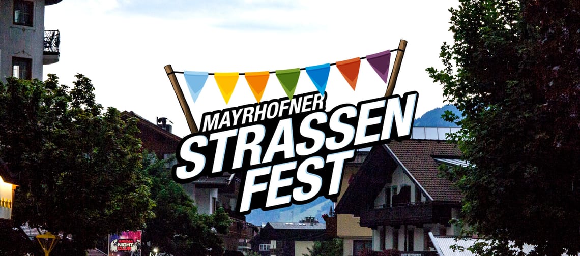 Auf diesem Bild wird die Mayrhofner Hauptstraße mit vielen Menschen gezeigt, ebenso ein Schriftzug mit Fahnen