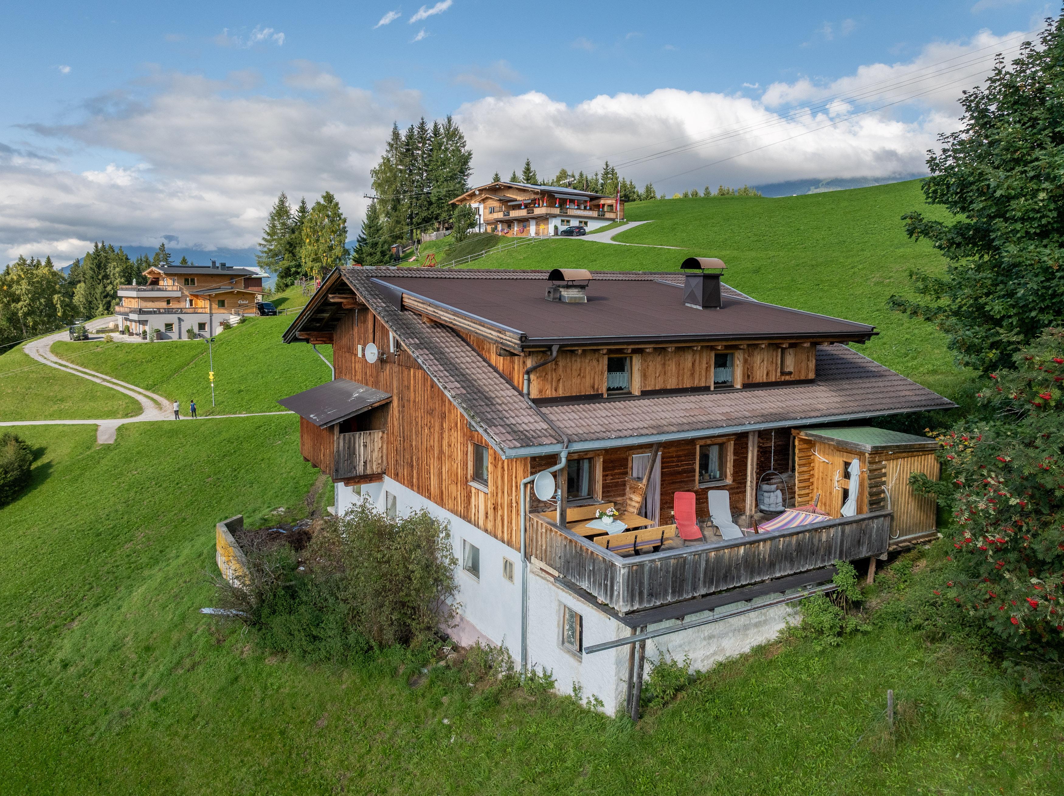 Häuser auf grüner Hügellandschaft mit Wiesen, Bäumen und einem blauen Himmel mit Wolken im Hintergrund.