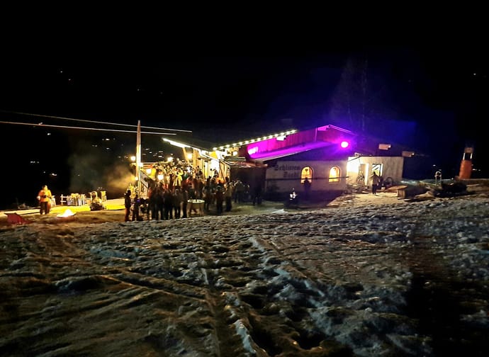 The picture shows the Schlittenstadl illuminated from the outside at night, with visitors.