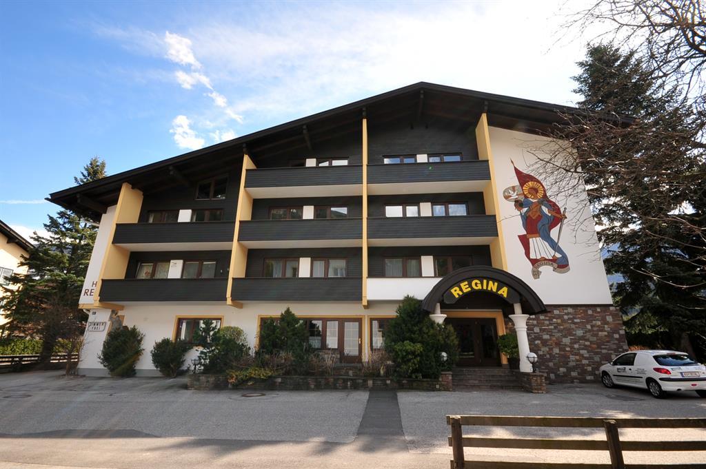Four-story hotel 'Regina' with a mural of a figure, trees, and parking in front.