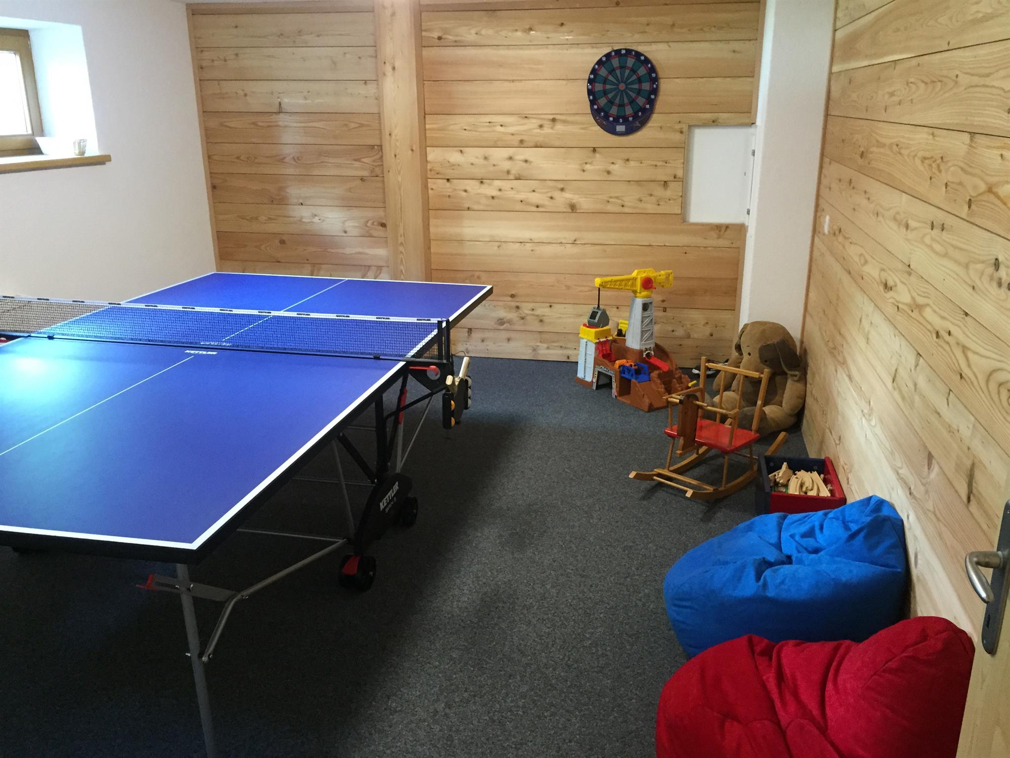 Game room with ping pong table, toys, and wood-paneled walls, window on the left.