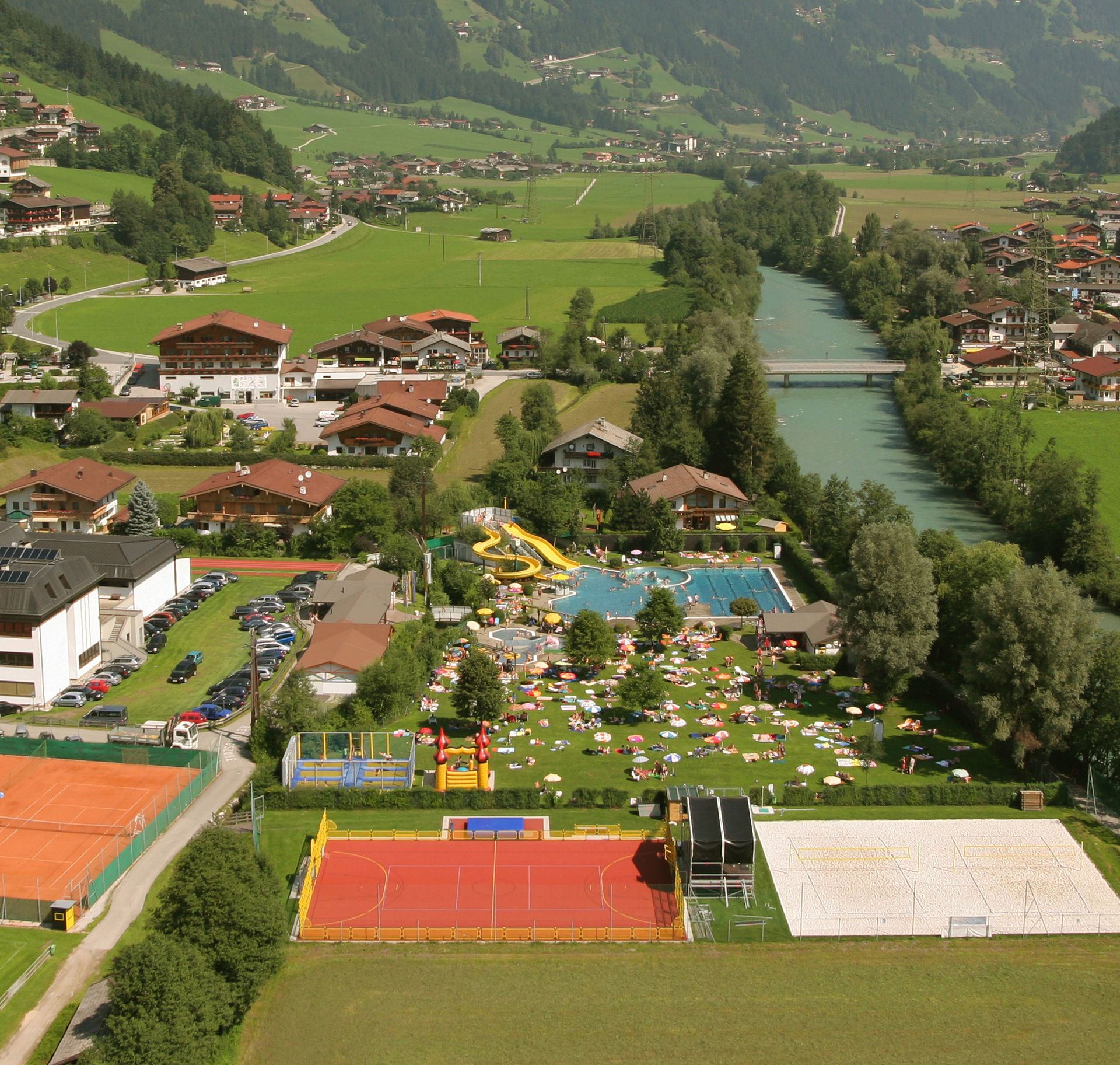 Aerial view of the Summerworld Hippach with outdoor pool, sports courts, and surrounding mountain landscape in Zillertal on a sunny summer day.