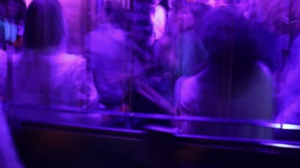 Dunkler Club mit tanzenden Menschen und bunten Lichtern, die eine lebhafte Atmosphäre schaffen.