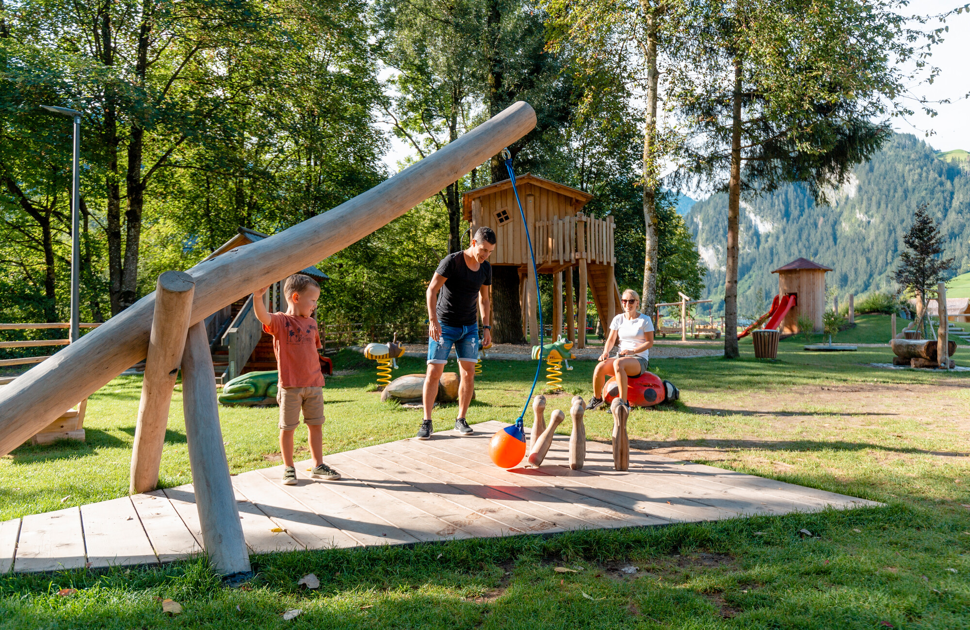 A family enjoys the nature-themed Auenland playground in Sidan, located in the Mayrhofen-Hippach holiday region – featuring wooden play equipment, treehouses, and plenty of space to play and relax in the green, surrounded by trees and mountains.