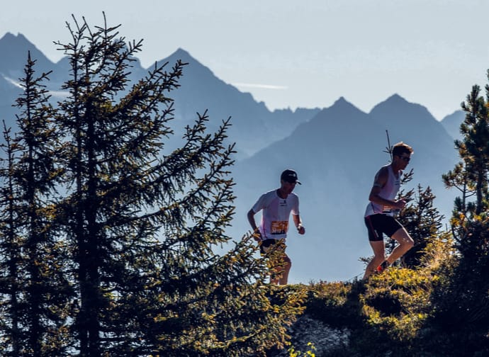 Two runners behind trees and in front of a mountain backdrop.