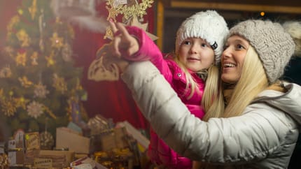 The image shows a mother with her child, who is showing him the Christmas decorations at a market.