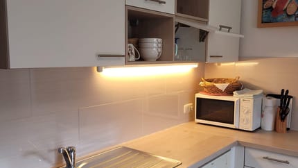 Küchenzeile mit Spüle, Mikrowelle, offenen und geschlossenen Schränken, Wandbild, und Küchenutensilien.
