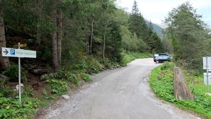 Parking lot in a forest with trees, cars, and a sign indicating hunting grounds.