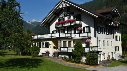 A multi-story house with white walls, black window frames, and colorful flowers on balconies.