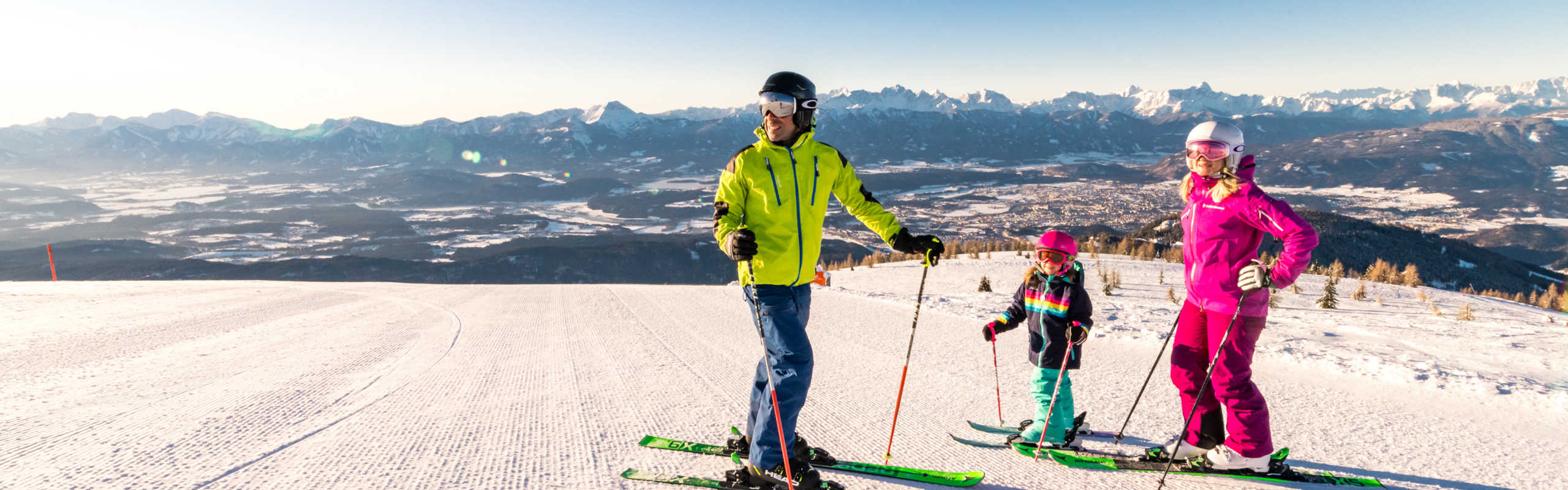 A family skiing on the Gerlitzen Alpe with a panoramic view of the Carinthian mountain landscape.