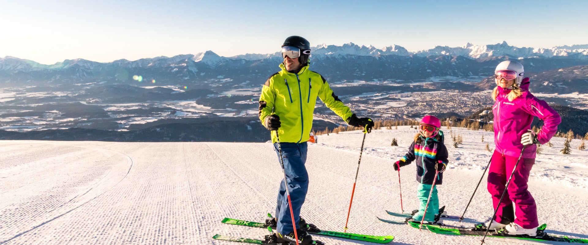 A family skiing on the Gerlitzen Alpe with a panoramic view of the Carinthian mountain landscape.