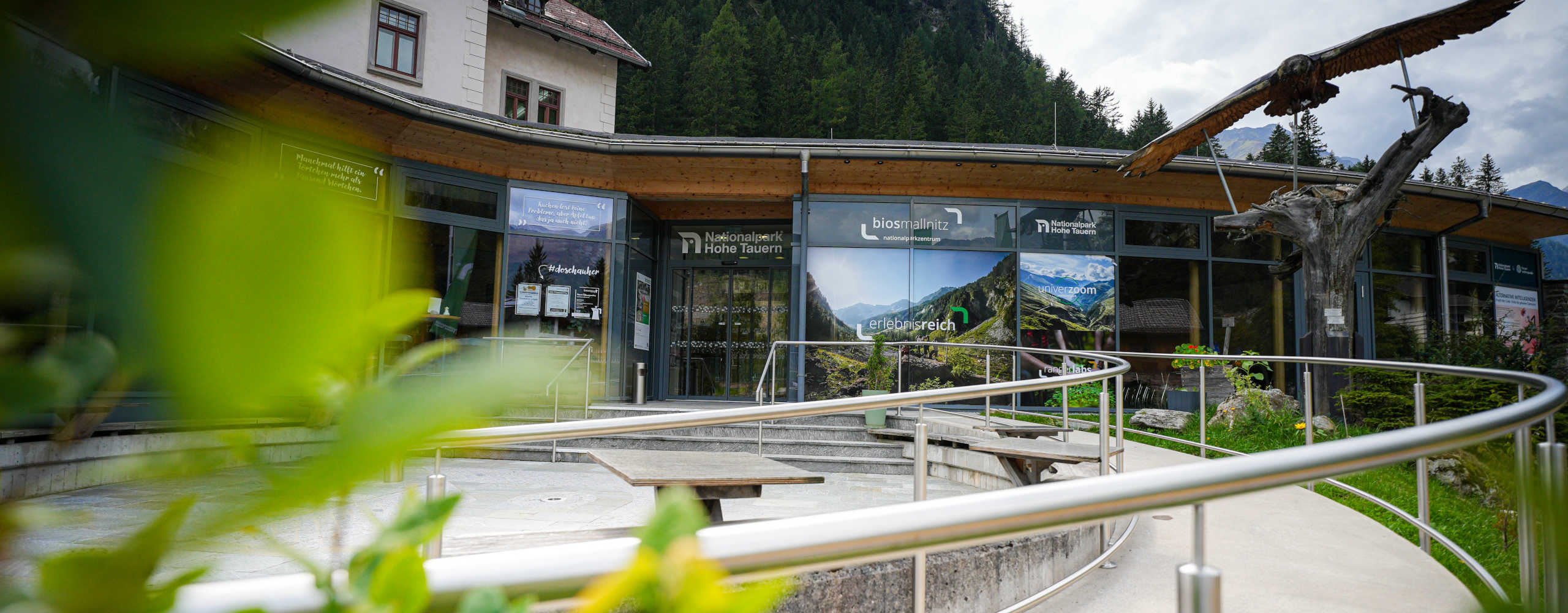 BIOS Nationalparkzentrum Mallnitz im Nationalpark Hohe Tauern mit modernem Eingangsbereich vor beeindruckender Berg- und Waldkulisse.