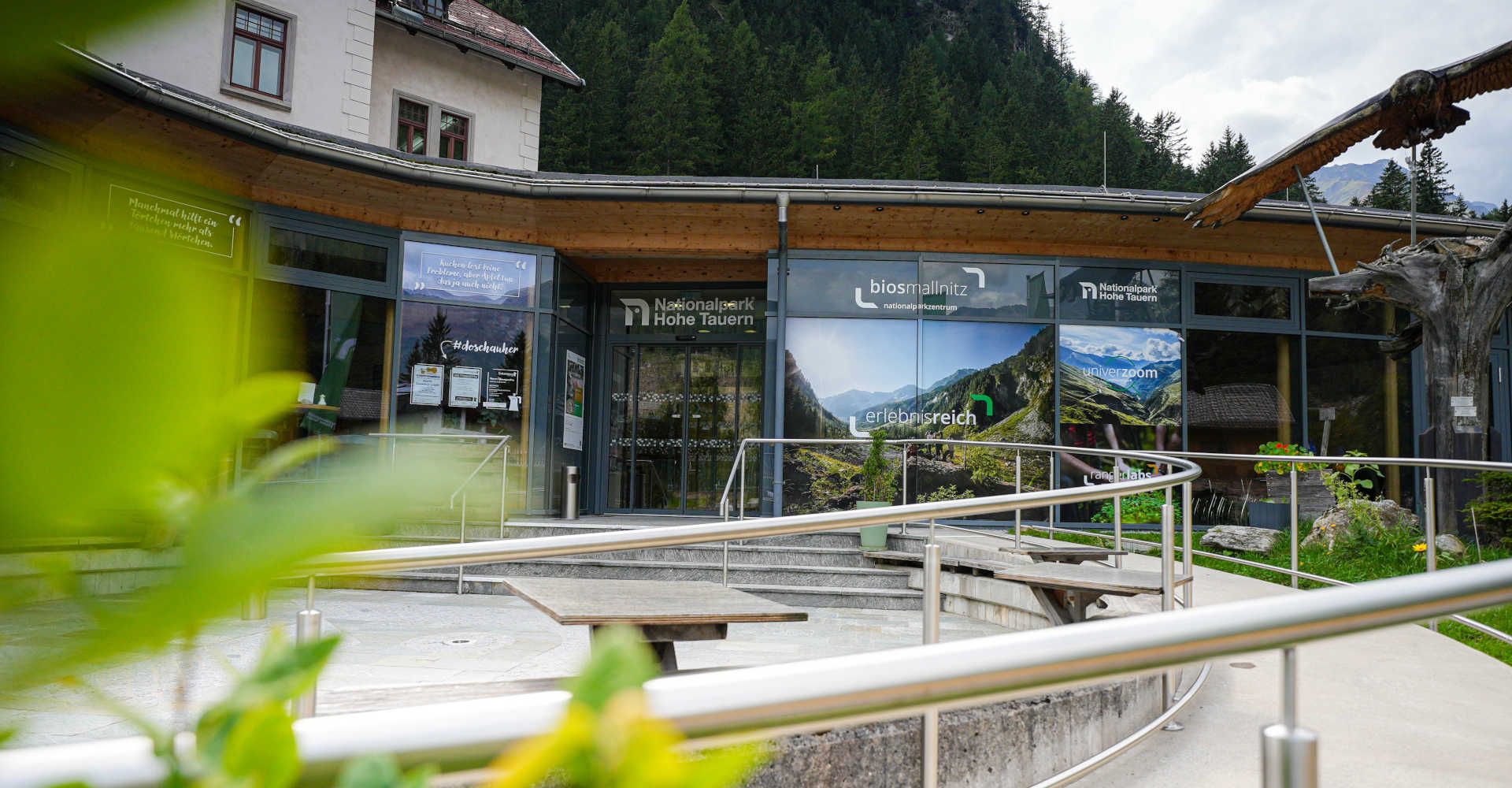 BIOS Nationalparkzentrum Mallnitz im Nationalpark Hohe Tauern mit modernem Eingangsbereich vor beeindruckender Berg- und Waldkulisse.