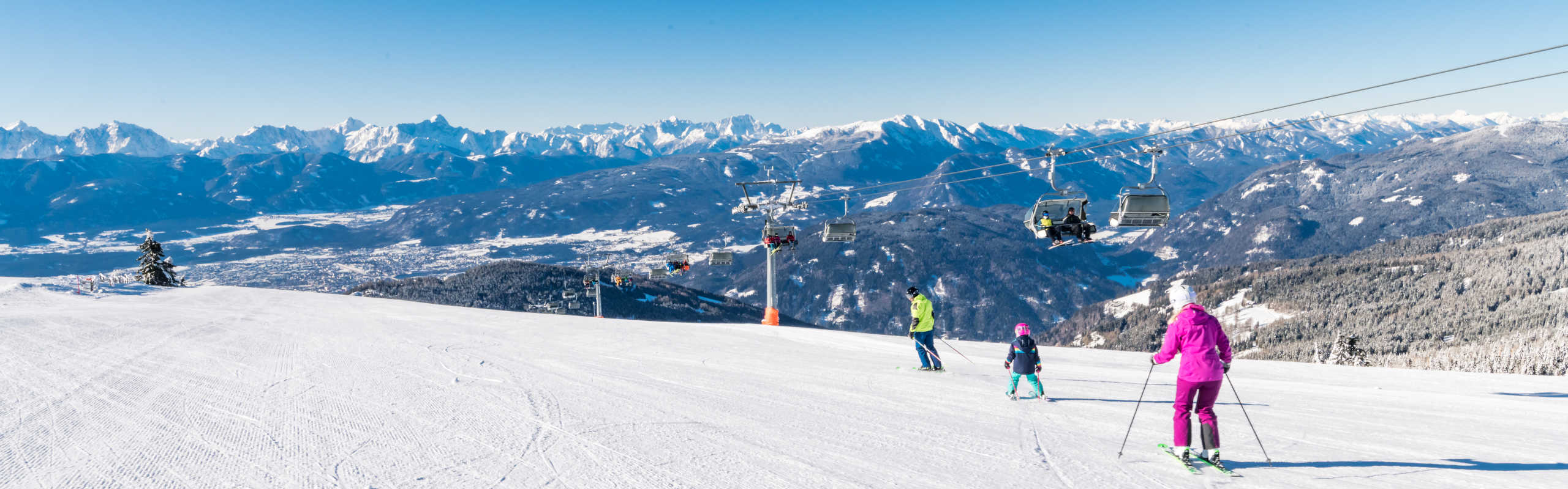 A family skiing on the Gerlitzen Alpe, riding the chairlift and enjoying a panoramic view of the Carinthian Alps.