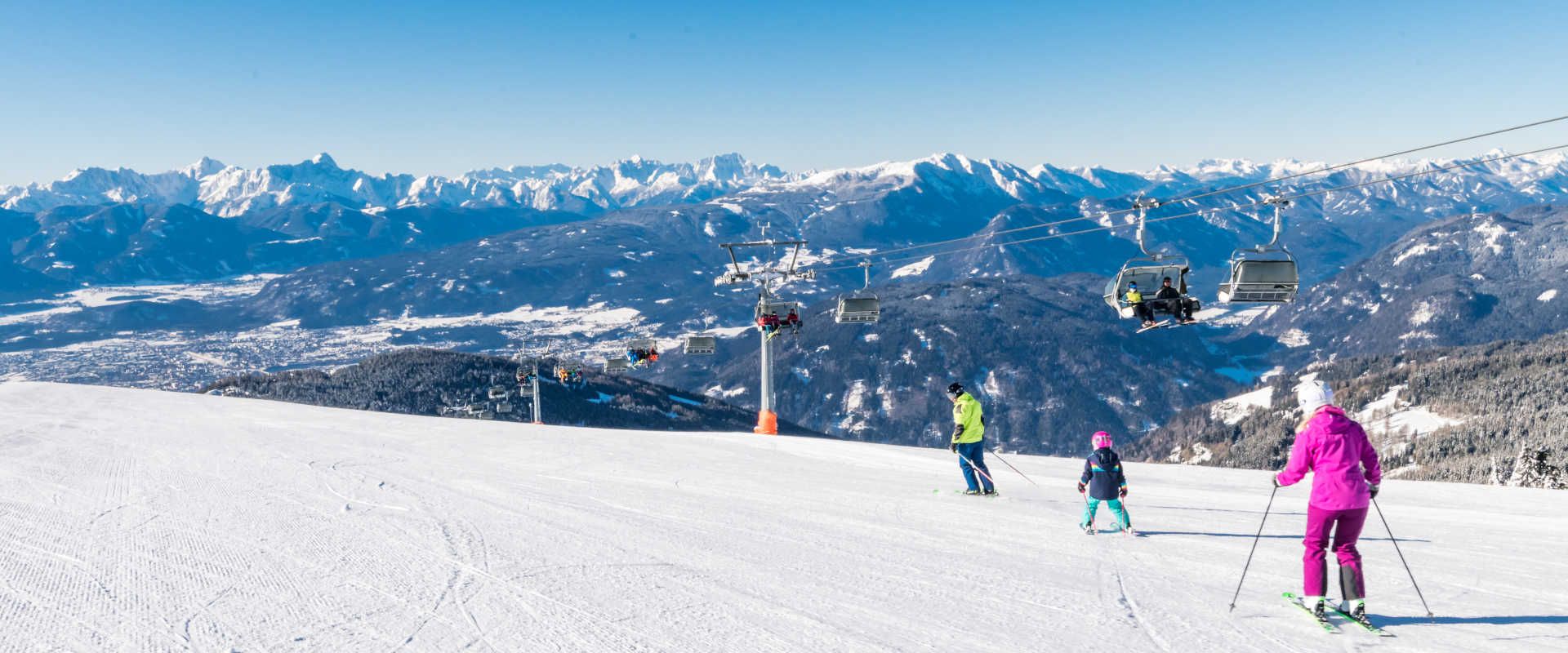 A family skiing on the Gerlitzen Alpe, riding the chairlift and enjoying a panoramic view of the Carinthian Alps.