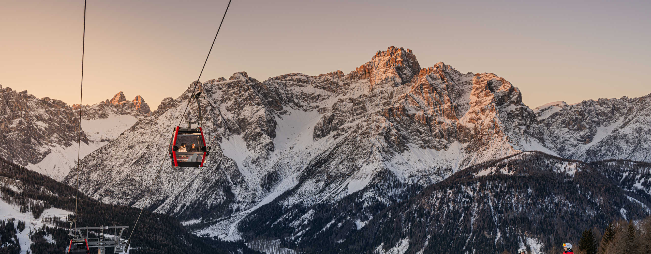 Seilbahn in den 3 Zinnen Dolomiten vor einer spektakulären, verschneiten Bergkulisse im Morgenlicht.