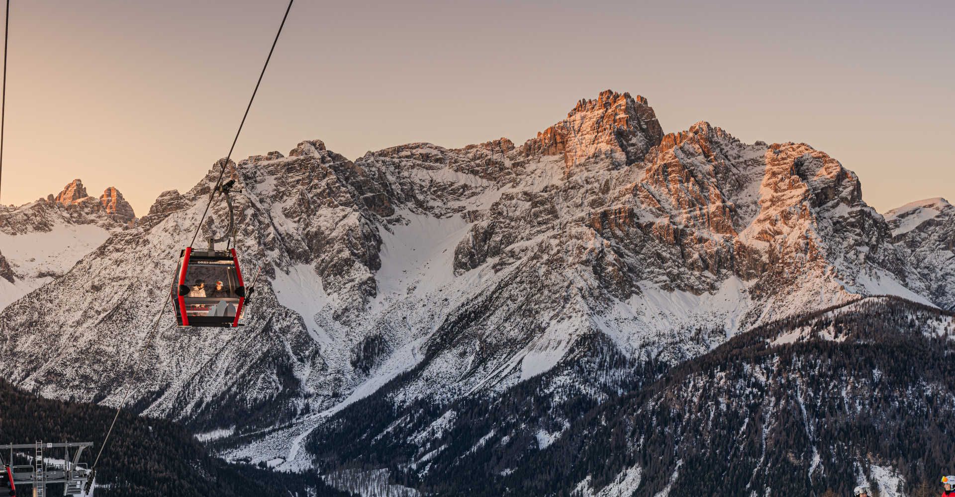 A cable car in the Three Peaks Dolomites against a spectacular, snow-covered mountain backdrop in the morning light.