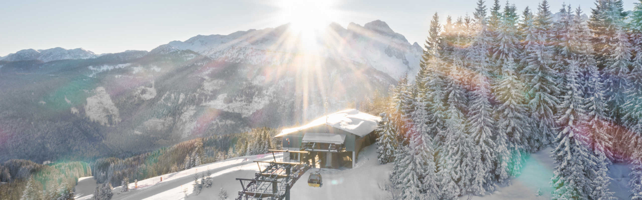 The Dachstein West Mountain Railway in winter, set against a backdrop of snow-covered Alps and a sunny mountain panorama.