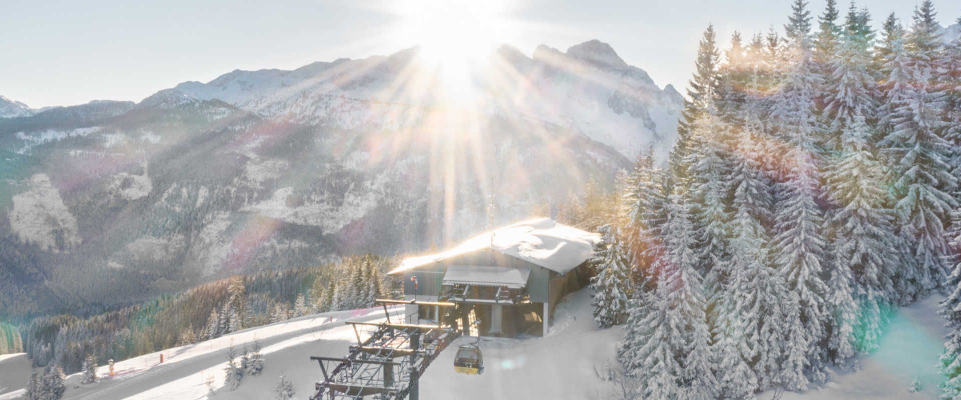The Dachstein West Mountain Railway in winter, set against a backdrop of snow-covered Alps and a sunny mountain panorama.