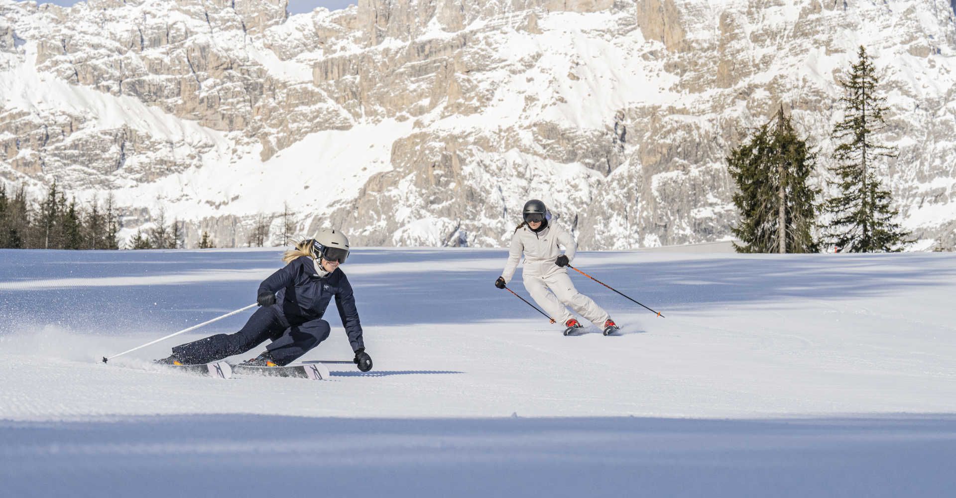 A skier on a perfectly groomed slope in the Three Peaks Dolomites against a stunning snow-covered mountain backdrop.