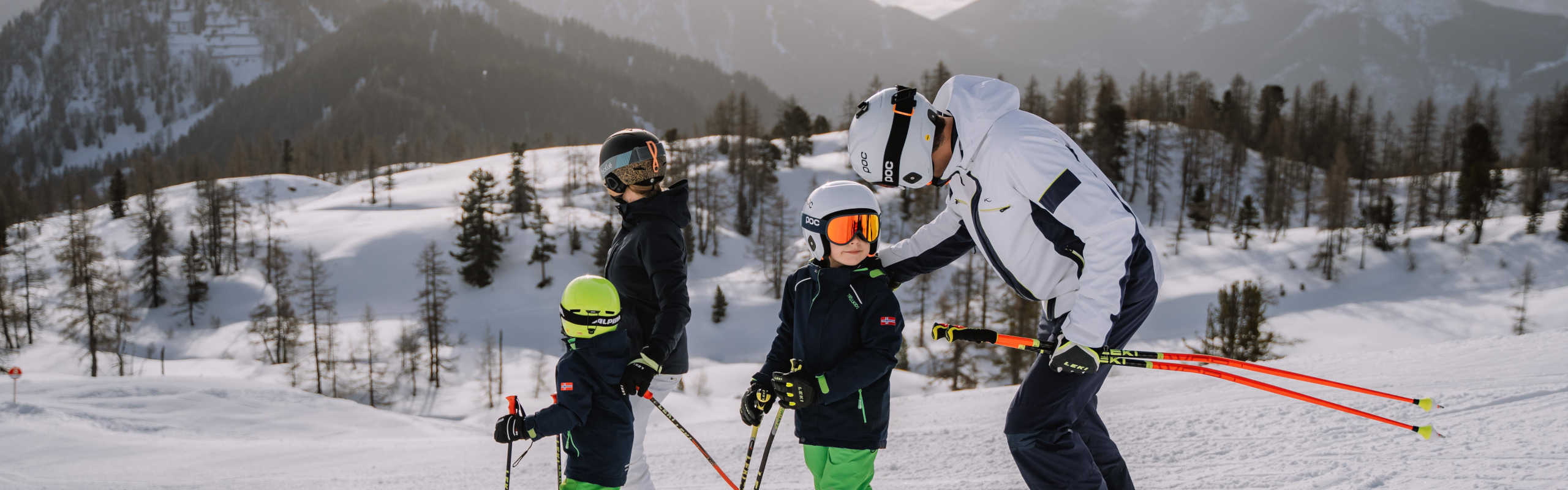 Family skiing at the Wurzeralm in Pyhrn-Priel, set against a backdrop of snow-covered mountains and a winter forest.