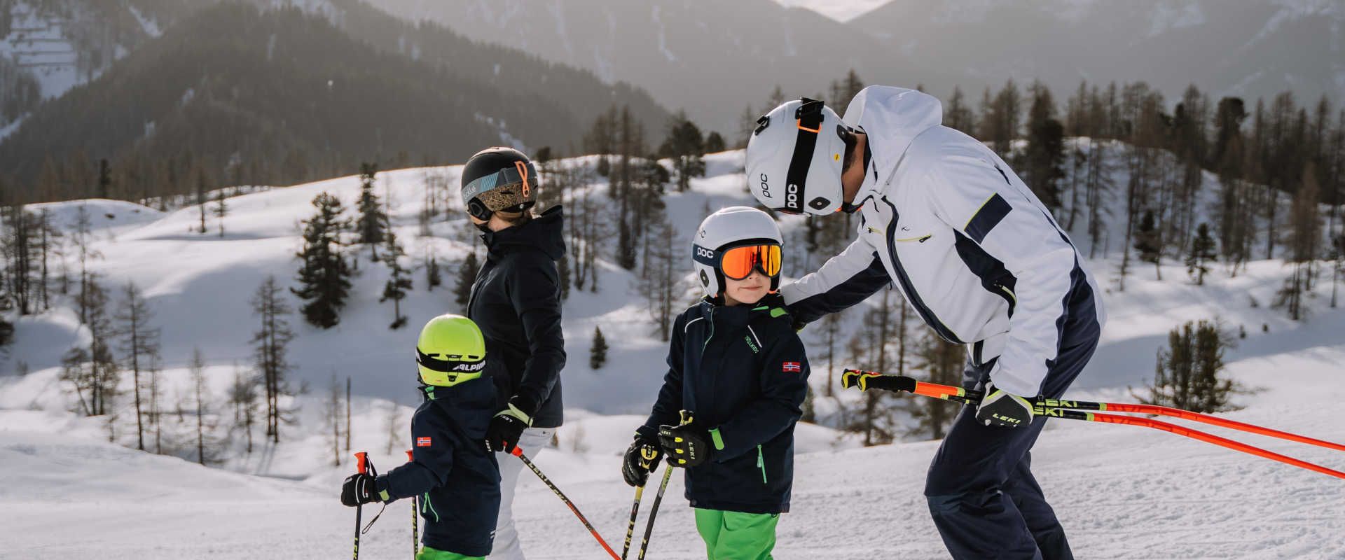 Family skiing at the Wurzeralm in Pyhrn-Priel, set against a backdrop of snow-covered mountains and a winter forest.